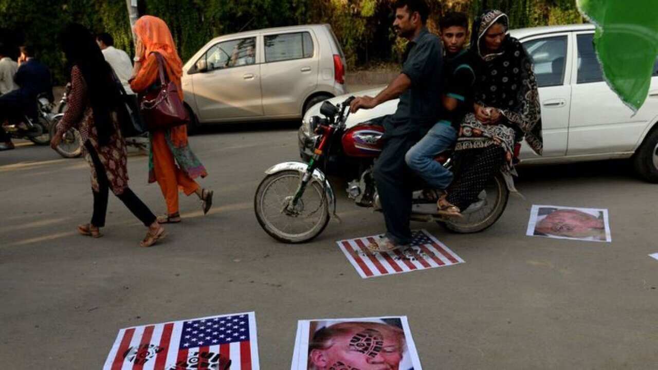 A Pakistani motorcyclist rides over images of US President Donald Trump and a US flag