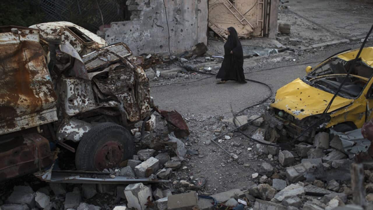 A woman walks past damaged vehicles in a neighbourhood of west Mosul