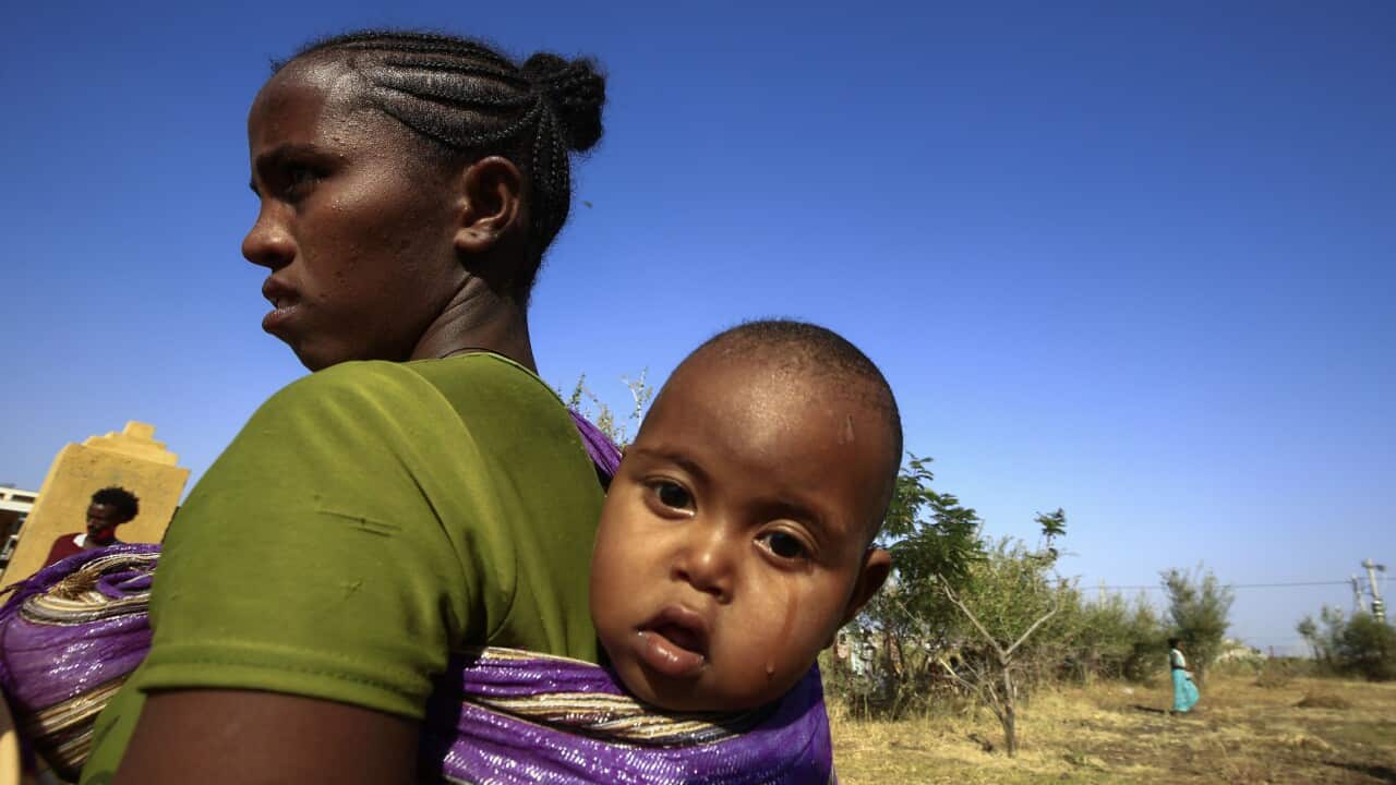 An Ethiopian refugee who fled fighting in the Tigray Region carries her baby on her back at the Village 8 border reception center in Sudan's eastern Gedaref State.