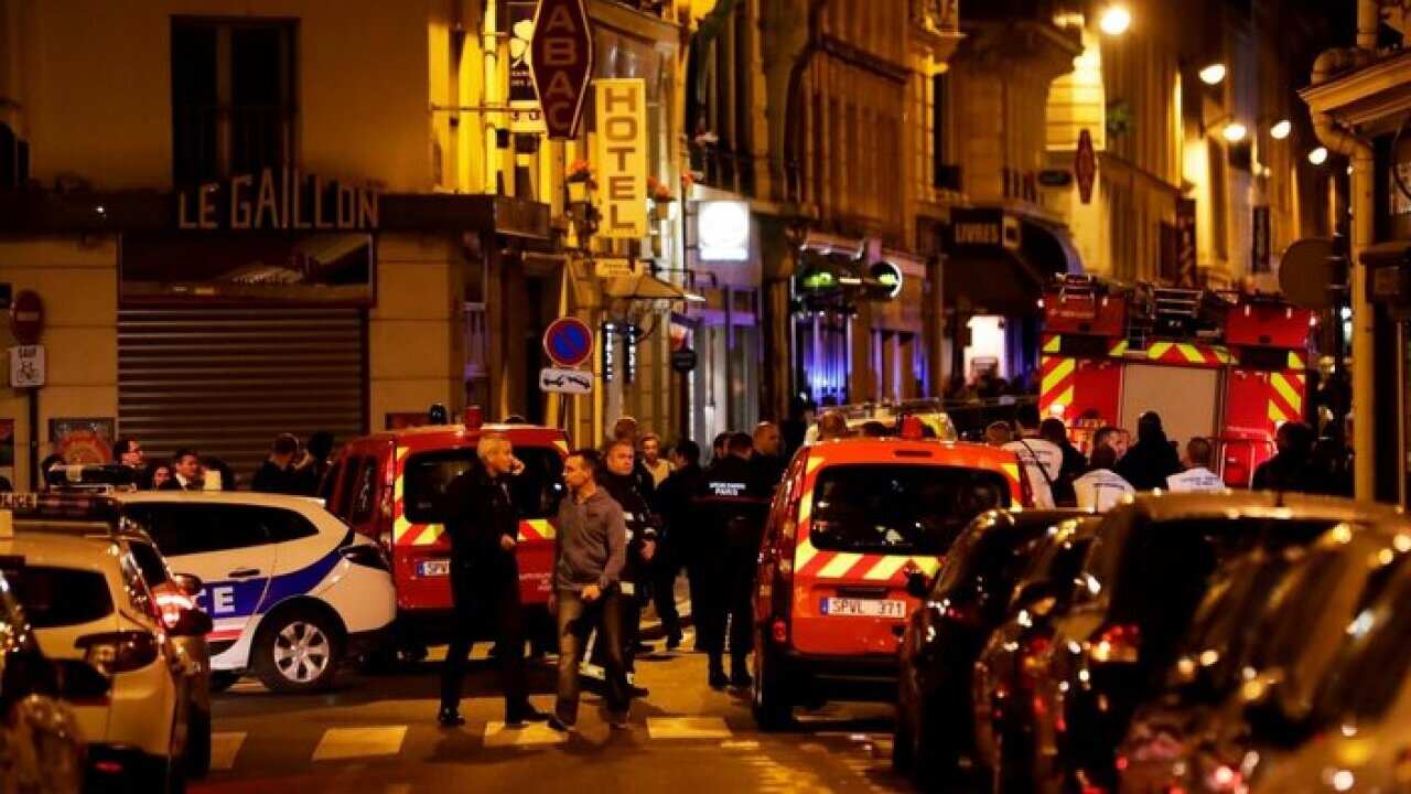 Policemen and emergency service members stand in a blocked street in Paris centre after one person was killed and several injured