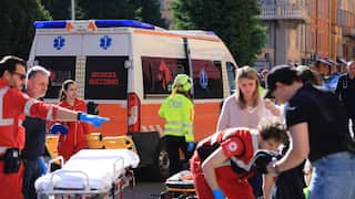 Paramedics and an ambulance roll stretchers toward people at an emergency scene. A small crowd of people look down at an injured person, who is out of frame.