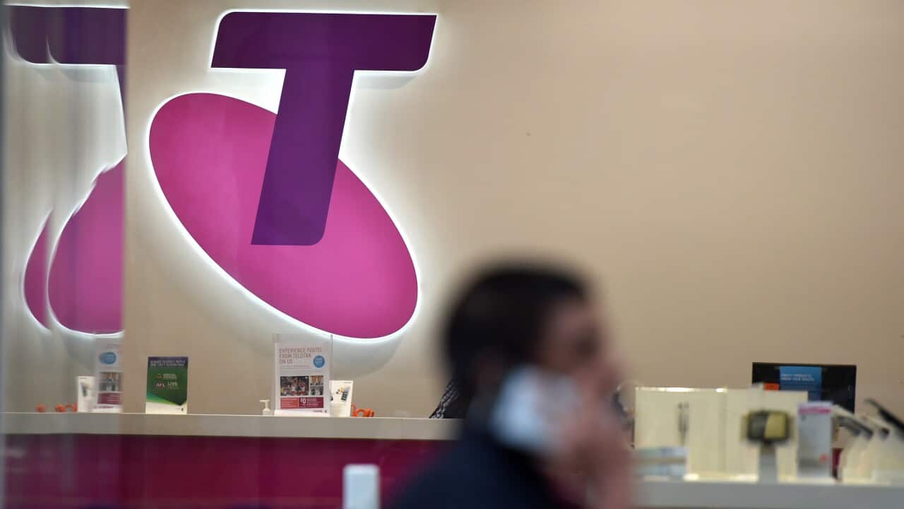 A man on his mobile walks past a Telstra store in Sydney.