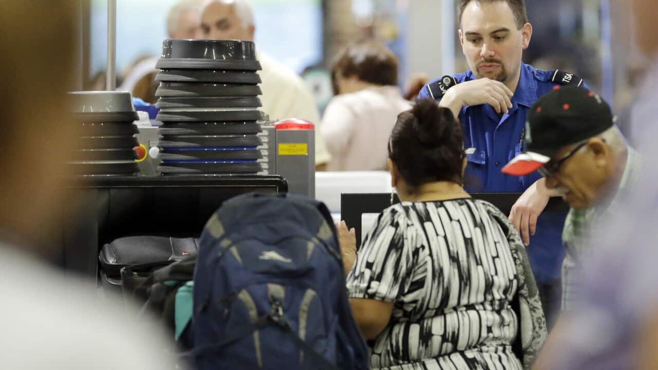 A TSA officer watches as passengers put their luggage through an X-ray machine at a TSA checkpoint at Miami International Airport.
