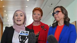 Three women stand together speaking into a microphone.