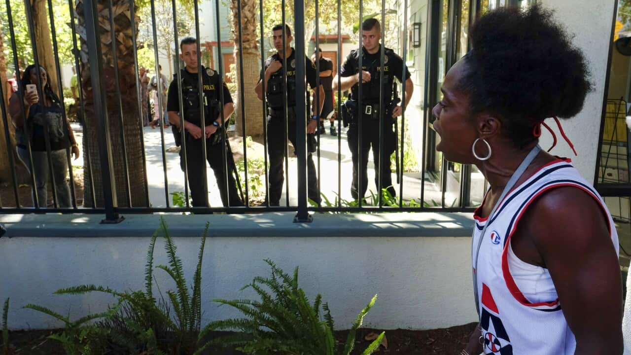 A protestor stands outside the front of Orange Grove Gardens as police stand guard during the investigation of the death of a black man.