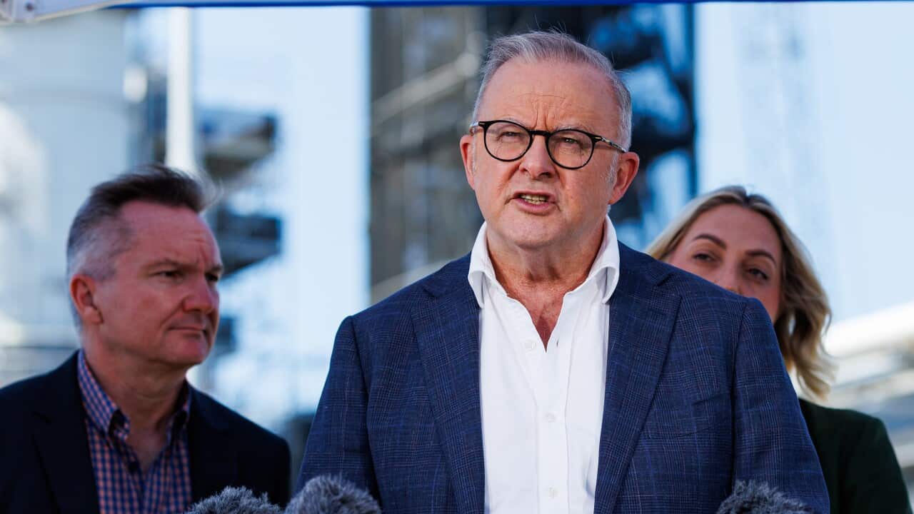 A man in a suit speaks with another man and a woman seen behind him
