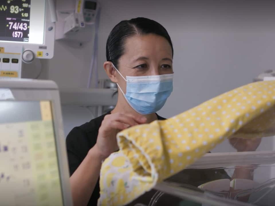 A female doctor stares into an incubator in a hospital.