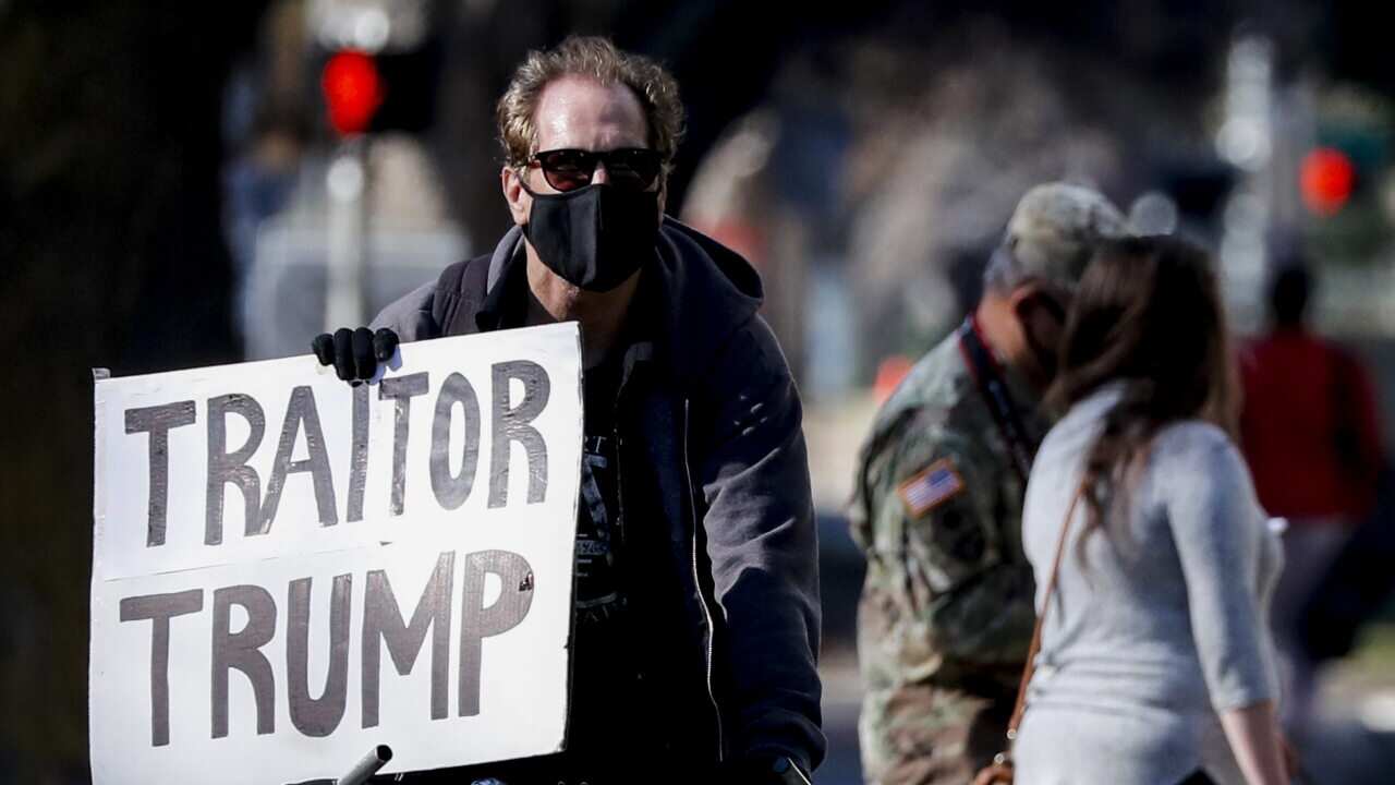 A man holding a sign reading 'Traitor Trump' next to California National Guard troops stationed around the state Capitol in Sacramento.