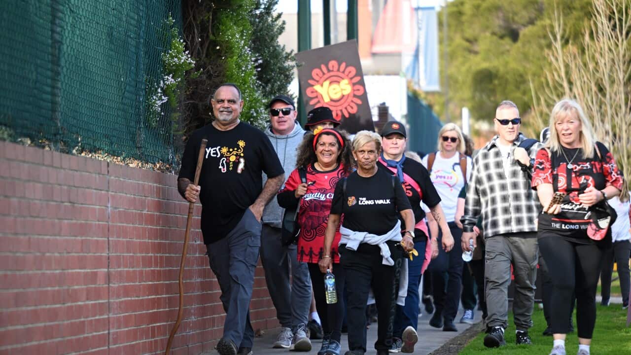 Michael Long (left) and supporters start the journey to Canberra from the Windy Hill Oval in Melbourne. A group of people walk along the pavement.