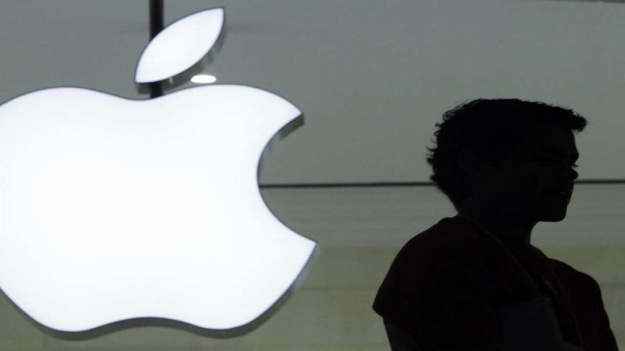 person stands near the Apple logo at an Apple store.
