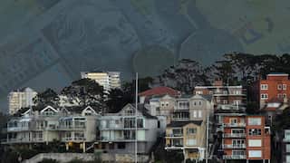 A graphic of Australian banknotes and coins faded behind a photo of seaside houses.