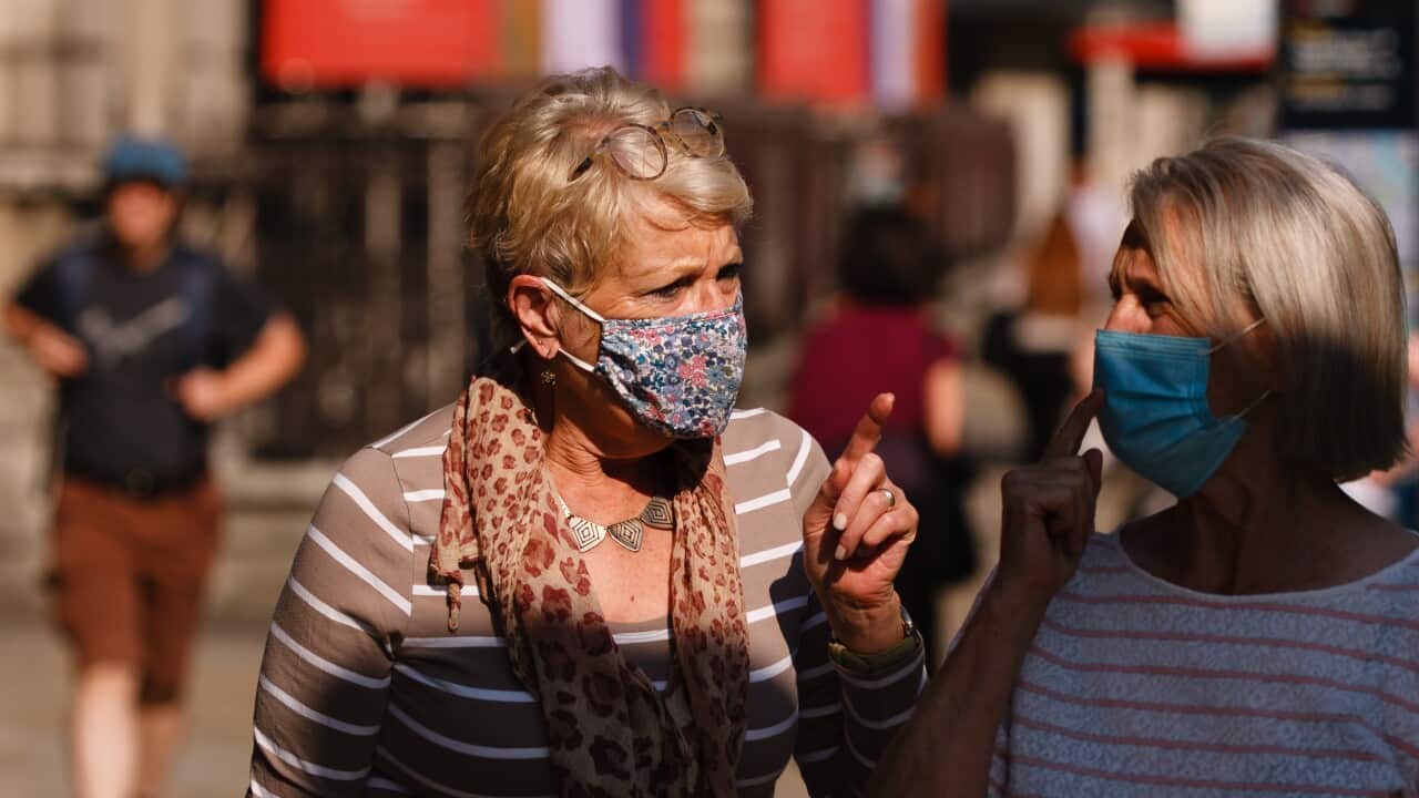 Two women wearing face masks speak to each other.