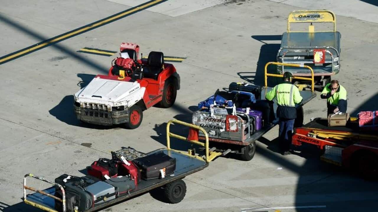 Baggage handlers unload luggage from a QANTAS plane