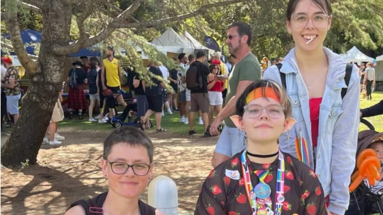 A person kneeling next to someone in a wheelchair and a third person standing