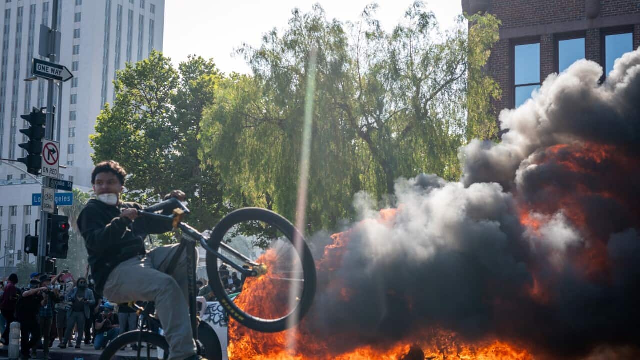 A cyclist, part of demonstrations in downtown Los Angeles, rides by an inflamed Taxi during protests against immigration raids June 08, 2025 AAP.jpg