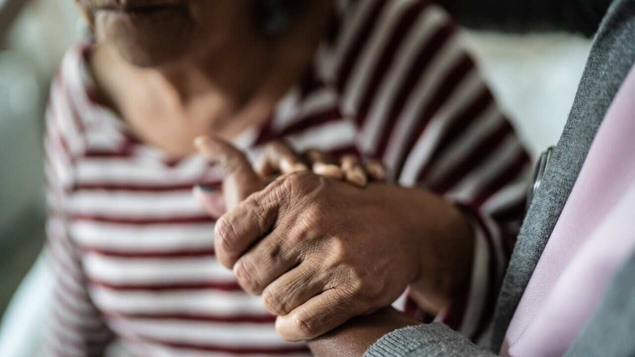Nurse or home caregiver and senior woman holding hands at home