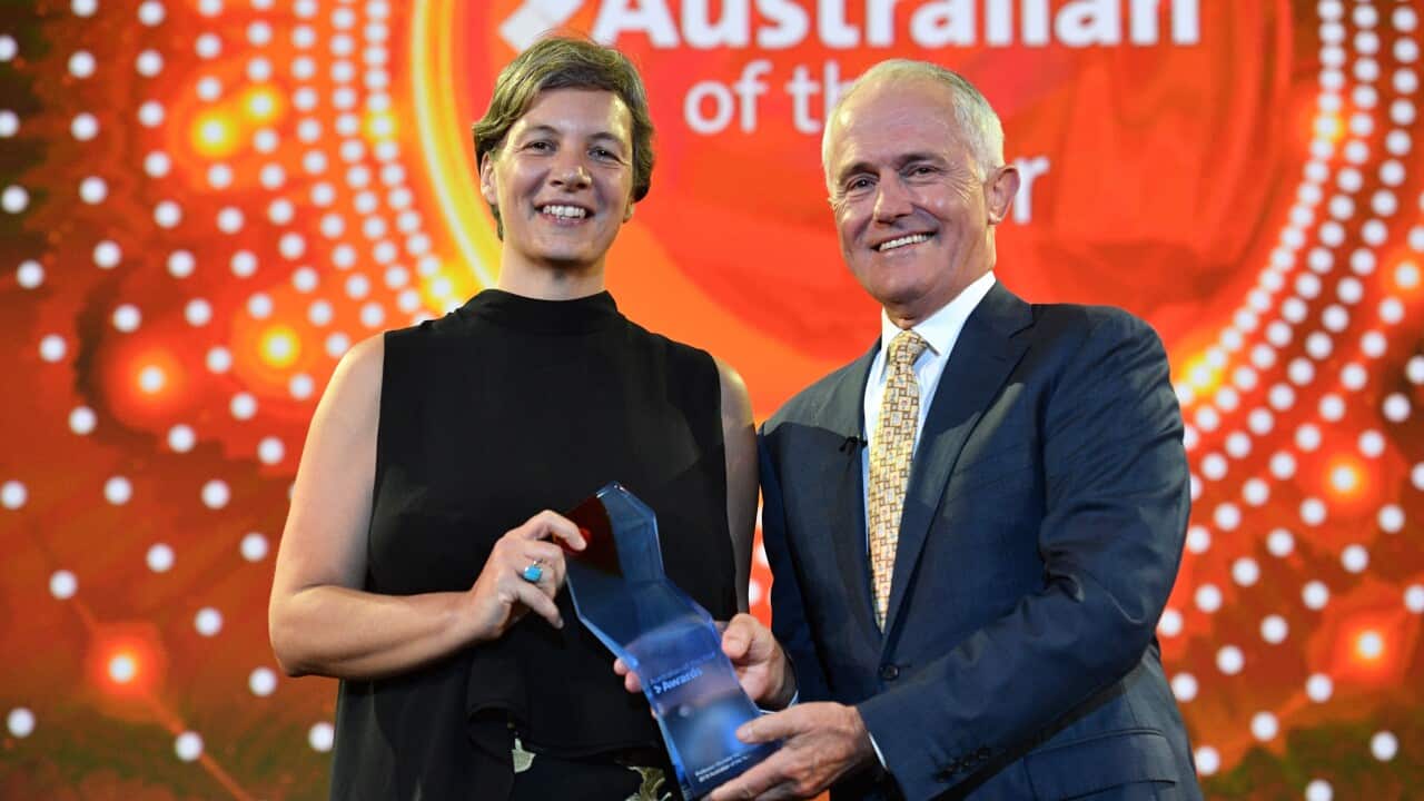 A man and a woman standing on a stage smiling while holding a trophy.