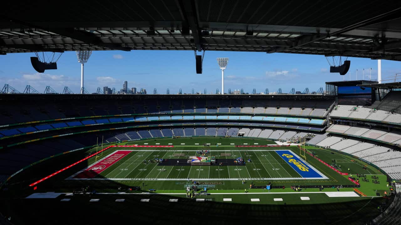 Wide view of a large stadium configured for an American football event, with team-branded end zones, a stage at midfield and mostly empty seating.