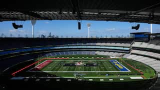 Wide view of a large stadium configured for an American football event, with team-branded end zones, a stage at midfield and mostly empty seating.