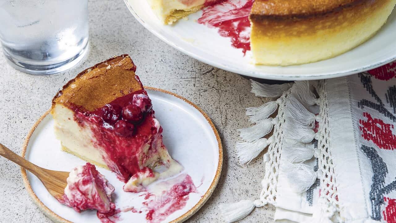 A cherry couli-topped cheesecake sits on a stand, with a piece from it on a plate in front.