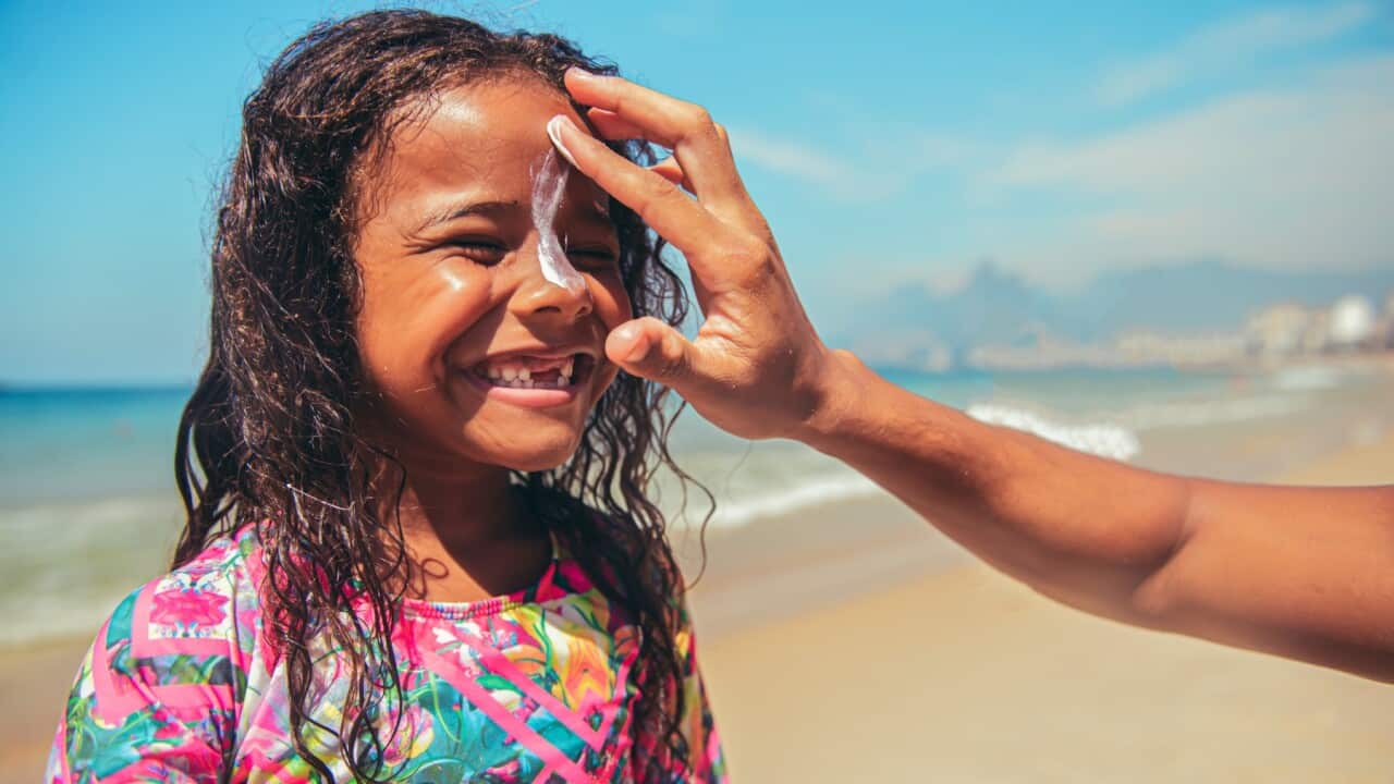 Little surfer girl preparing for surf with suntan lotion on a face