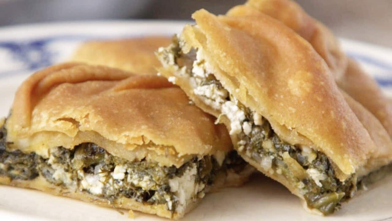 Two pieces of spanakopita, with thick golden pastry and a cheese and greens filling, sit on a blue and white plate.