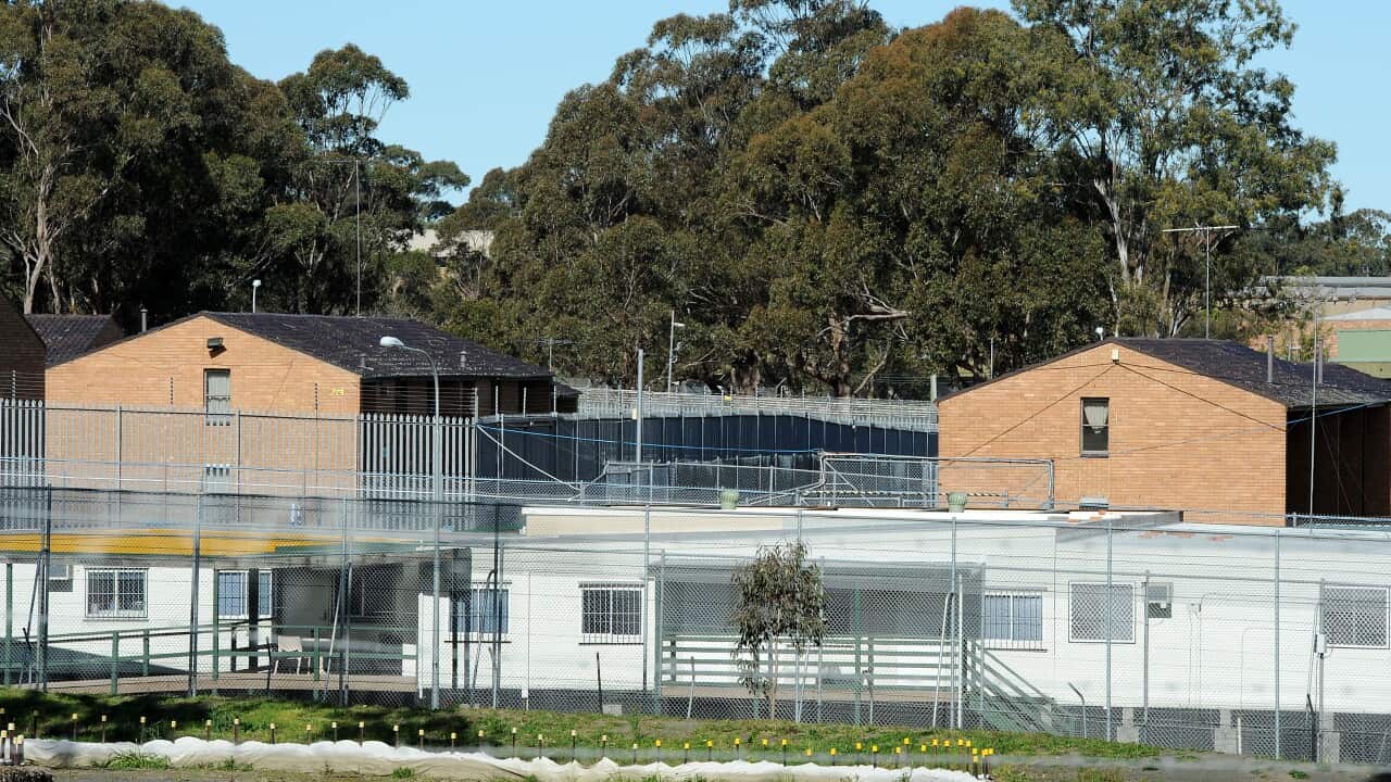 Two red brick buildings with a fence in front of them.
