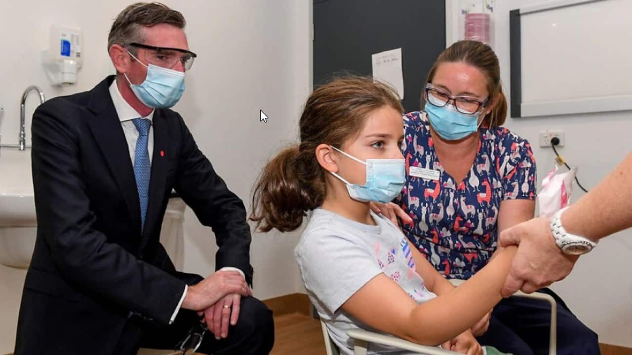 NSW Premier Dominic Perrottet watches on as Ines Panagopailos, 8, receives her first dose of the COVID-19 vaccination at the Sydney Children’s Hospital.