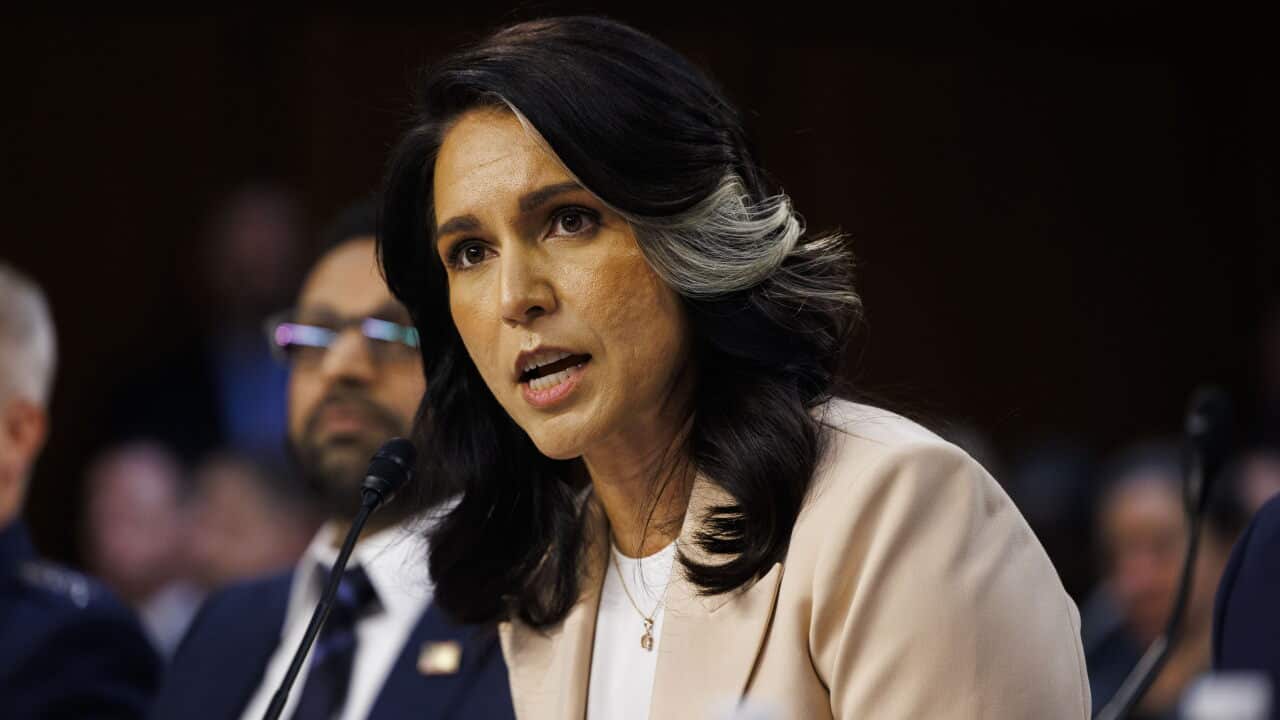 Woman speaking into a microphone during a formal hearing or committee session.