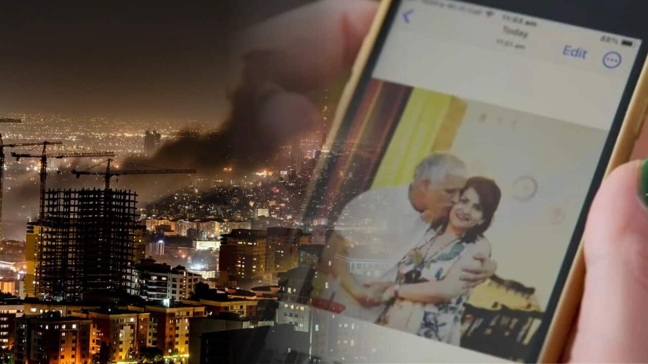 A composite image of a hand holding a photo with two people on it, and smoke rising from a city's buildings.