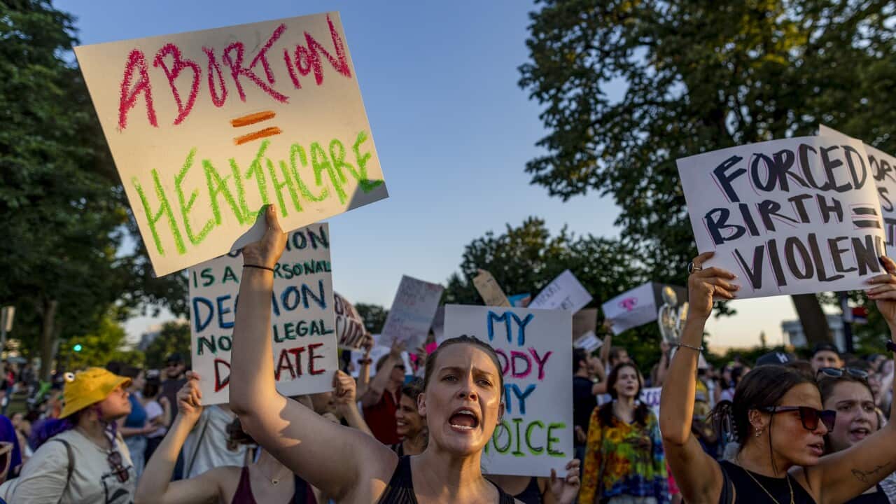 Women carry placards with large words on it. One says, 'abortion = heathcare'. The other says, 'forced birth = violence'.