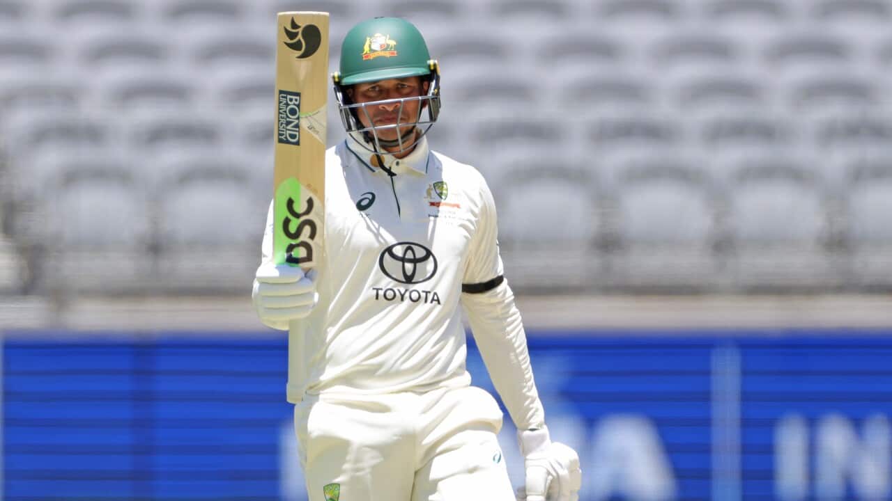 A person wearing white cricket uniform carrying a bat with a black armband
