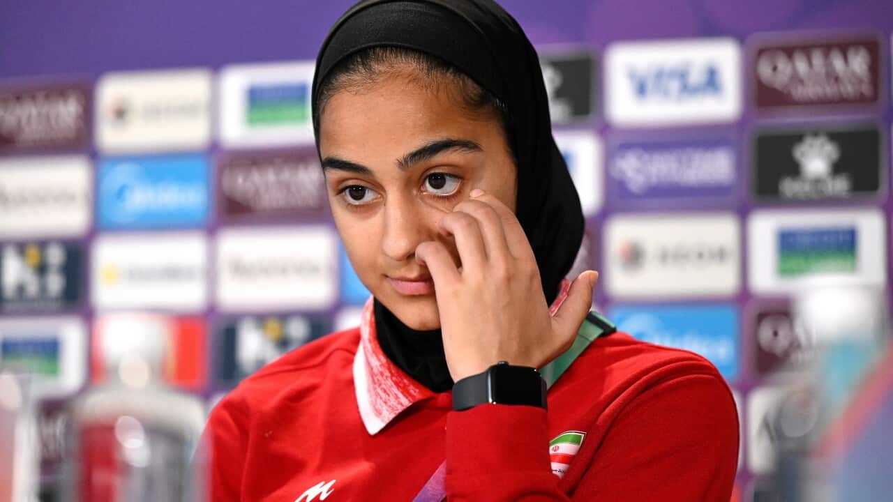 Iranian football player Sara Didar at a press conference for the 2026 AFC Women's World Cup. She is dressed in Iran's red team kit and appears to be wiping a tear from her eye.