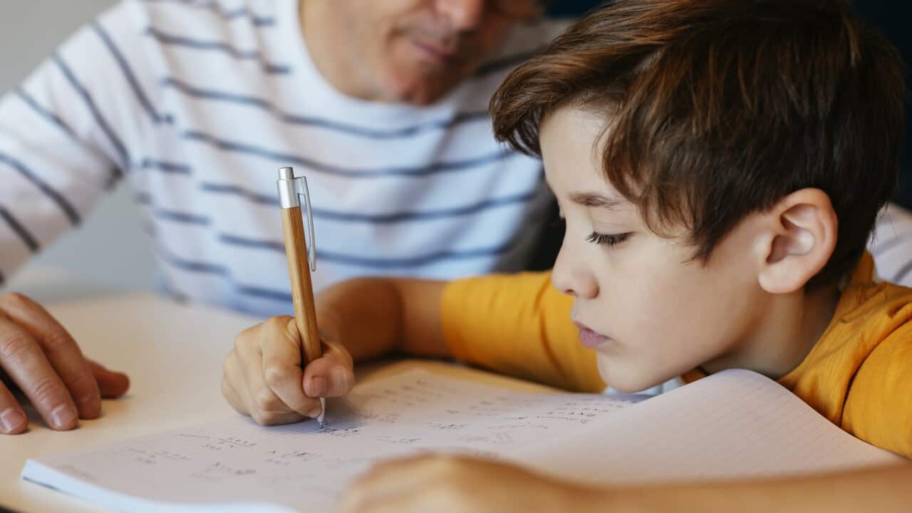 Father watching son doing homework at table