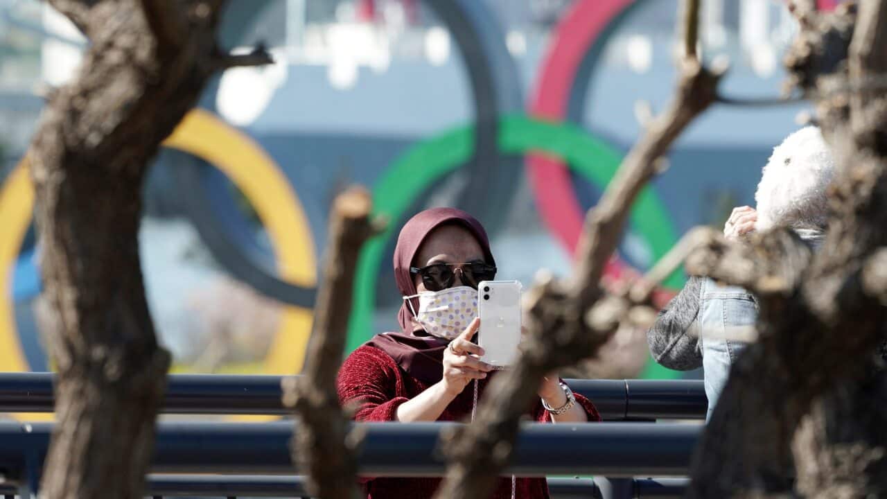 A tourist wearing a protective mask takes a photo with the Olympic rings in the background, 3 March, 2020, in Tokyo.