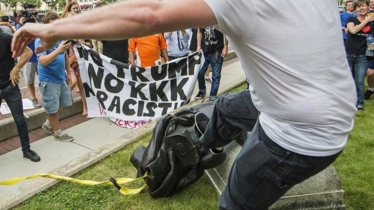 A protester kicks the toppled statue of a Confederate soldier