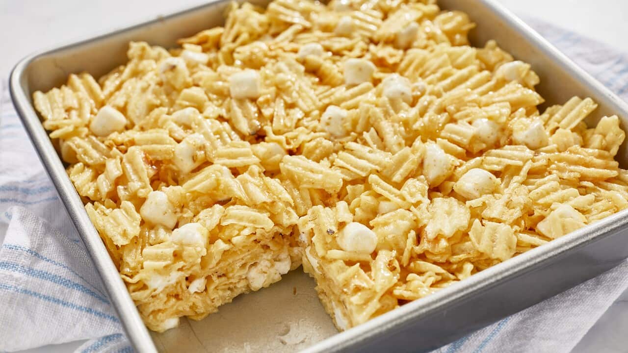 A metal baking tray holds a layer of baked potot chips, studded with small marshmallows. One piece has been removed, showing the interior.