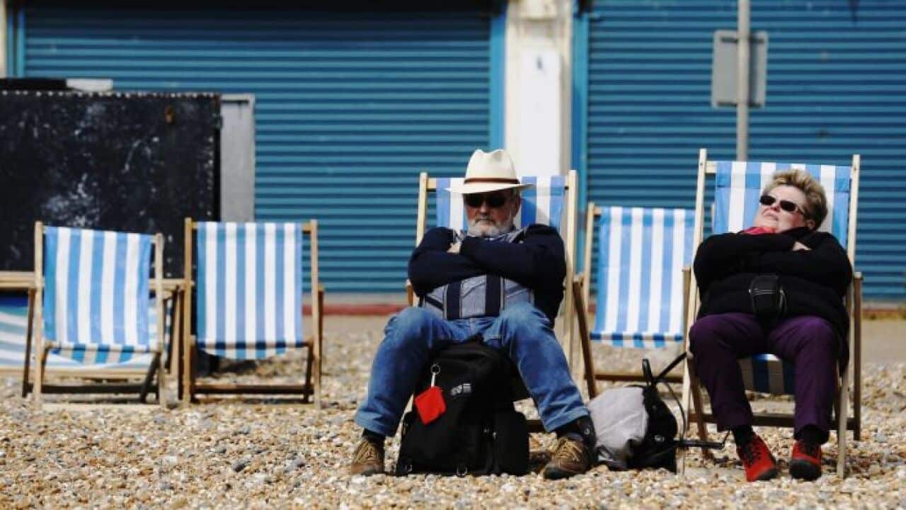 An elderly couple sits on deck chairs on a cool afternoon