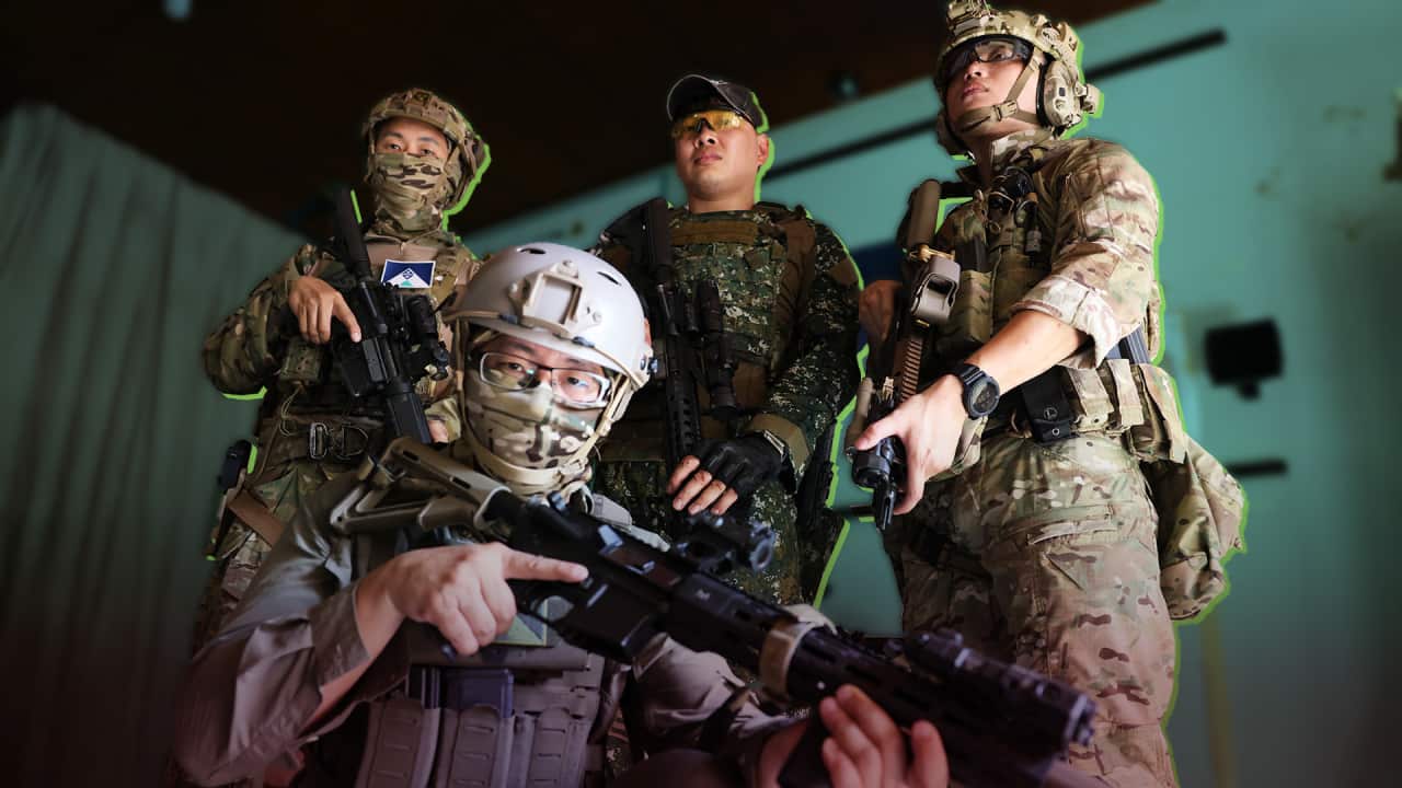 Four Asian men in full combat gear and holding air guns pose for a photo