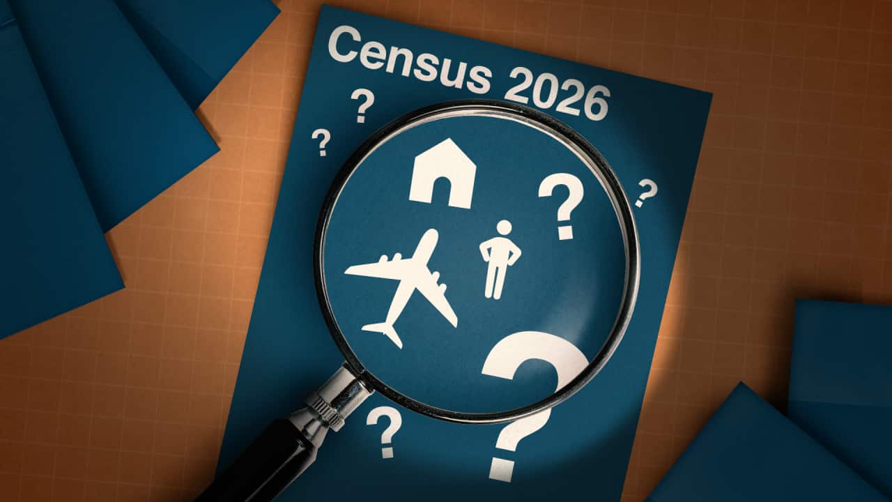 A magnifying glass hovers over a blue piece of paper with various white icons and question marks. The paper includes the text Census 2026.
