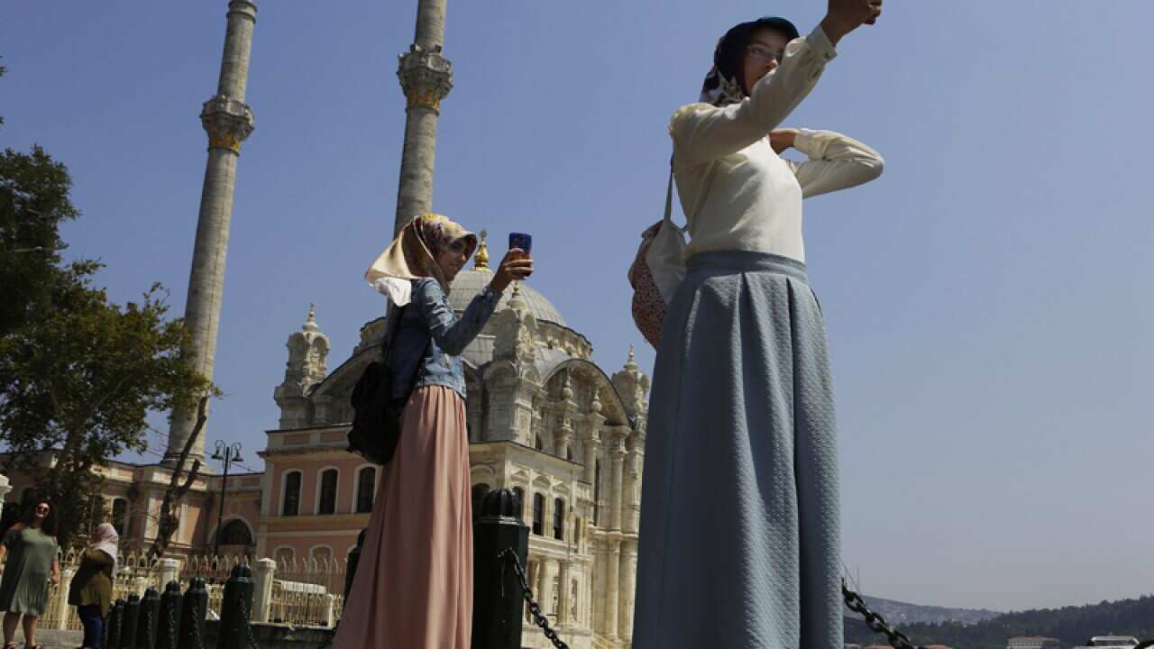 Women take photos outside the Ortakoy Mosque in Istanbul, Turkey