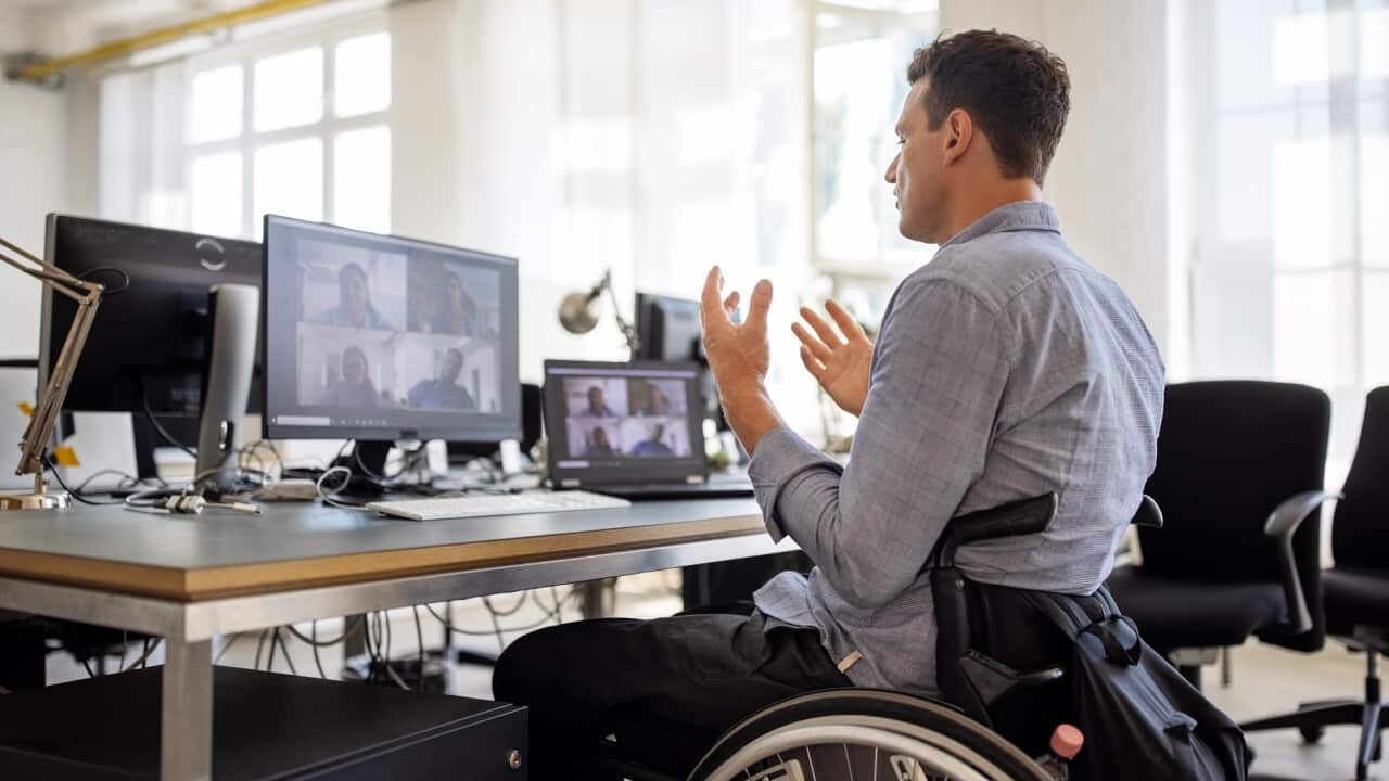 Businessman on a wheelchair having a web conference on his computer at creative office desk.