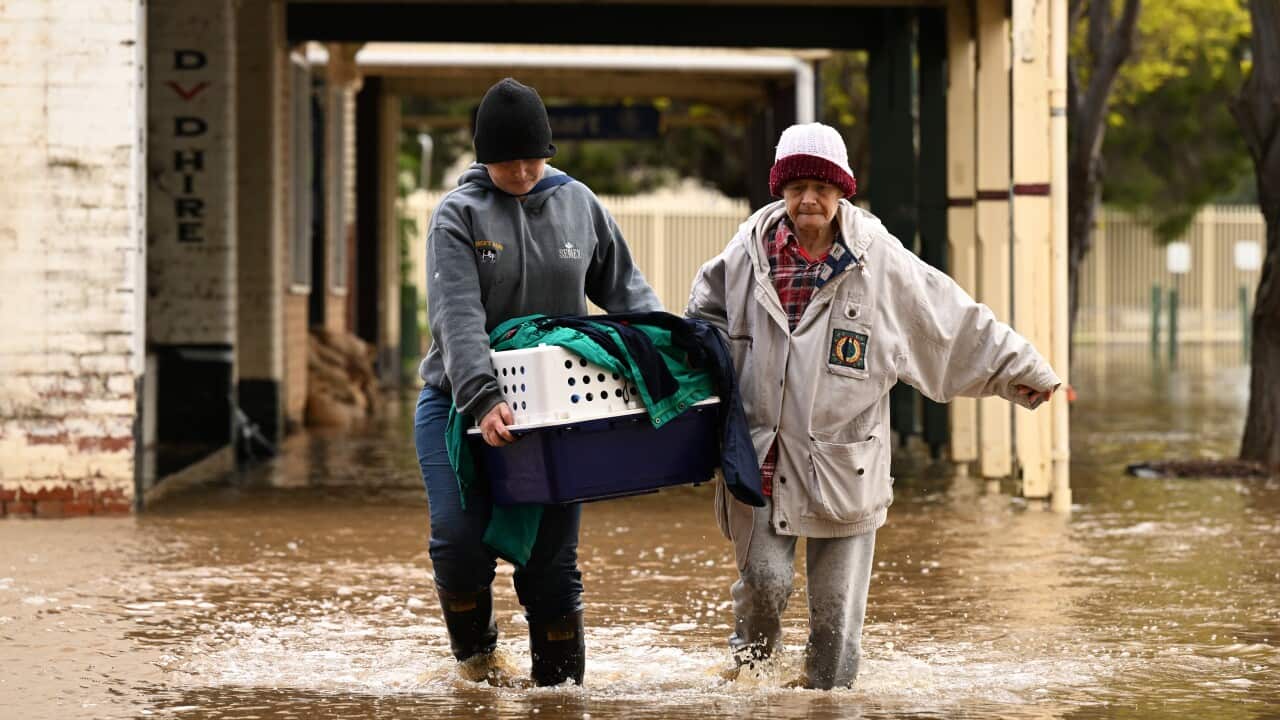 Two woman walk through floodwaters holding a pet carrier