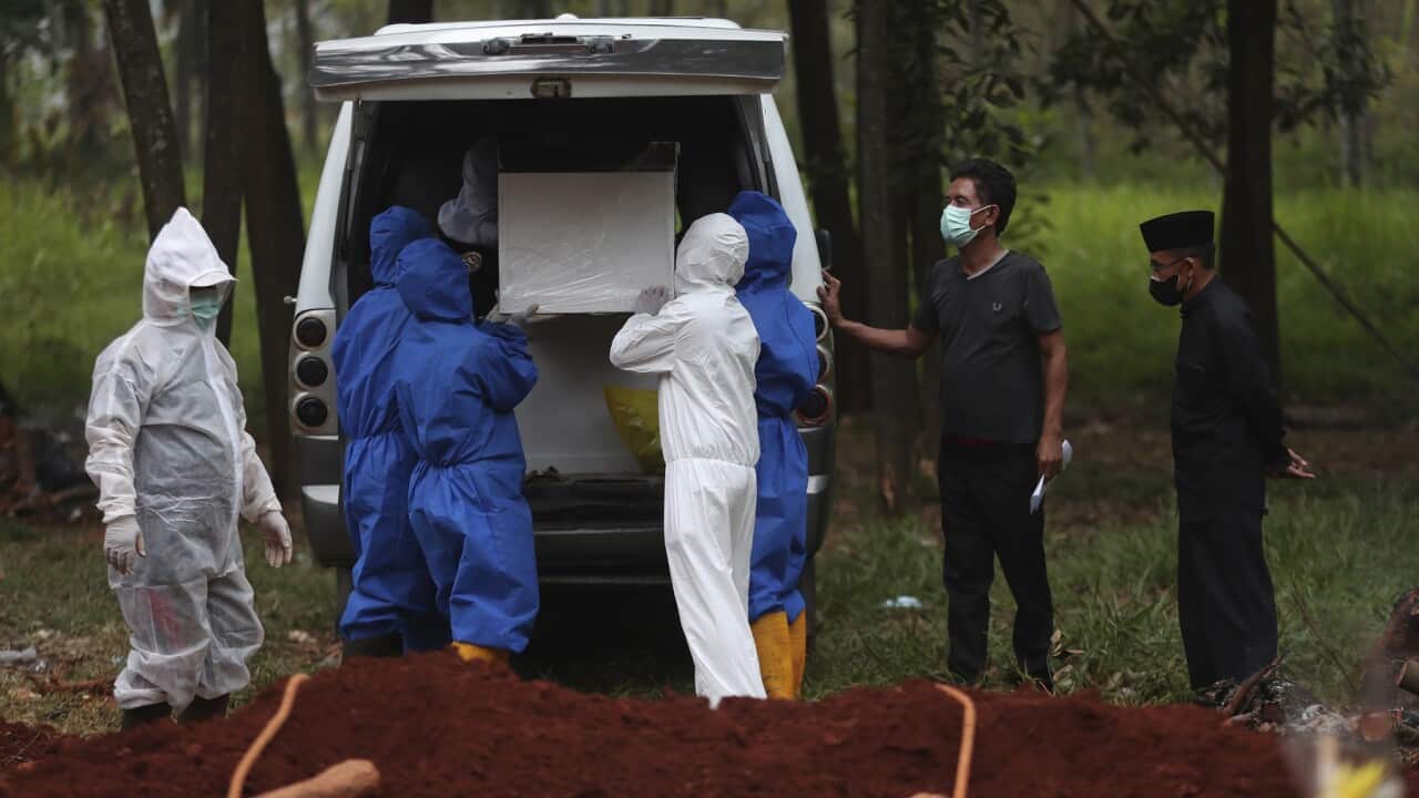 Workers in Indonesia in protective suits remove a coffin containing the body of a COVID-19