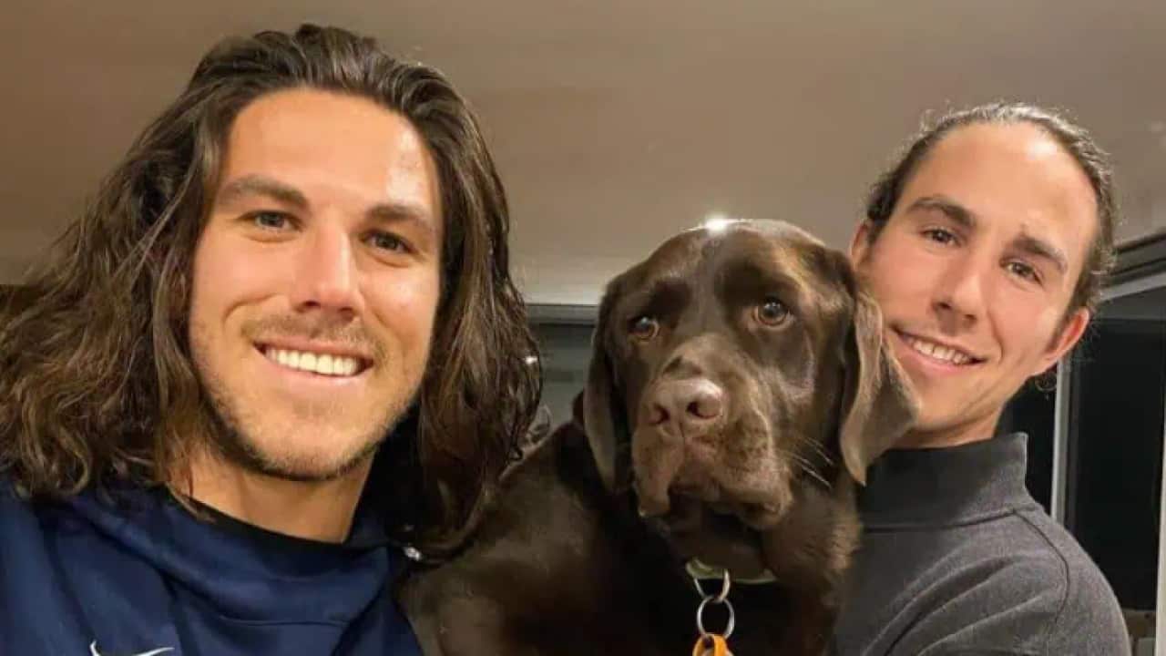 Two men with brown hair posing for a photo with a brown dog.
