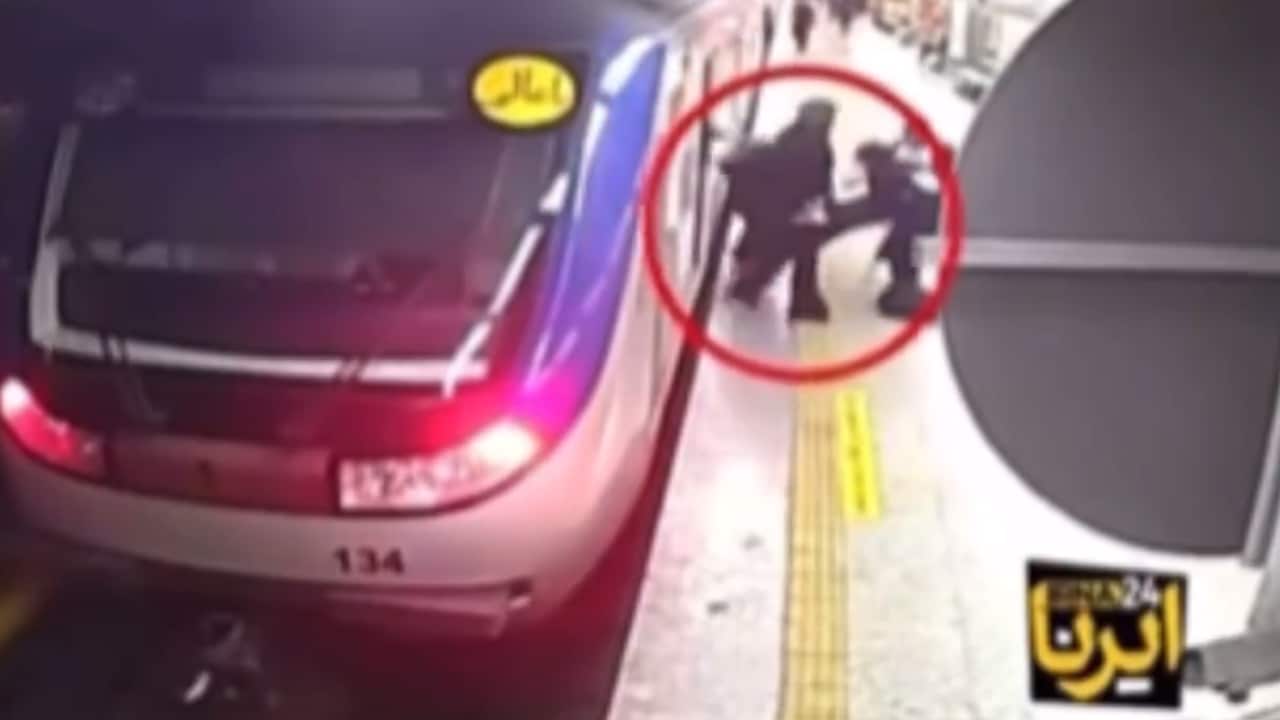 CCTV screenshot image of two figures on train platform, standing close to the edge near the train itself in what appears to be an altercation.