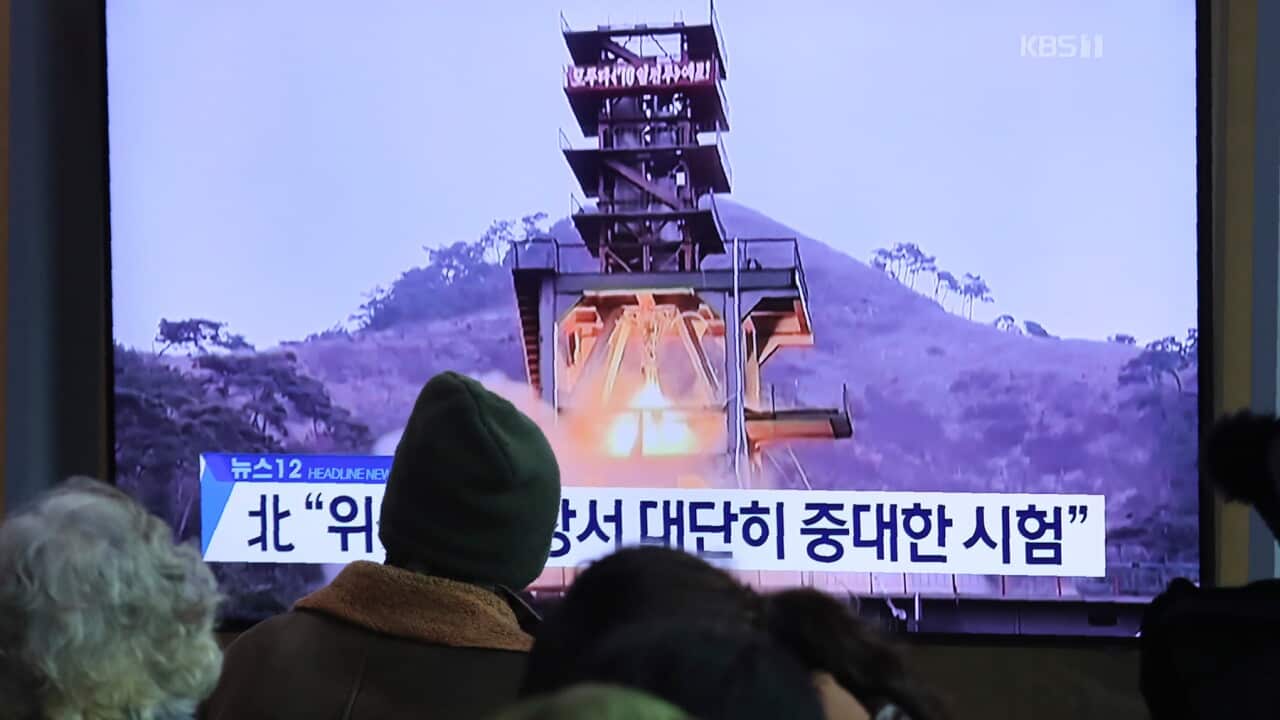 People watch a TV screen showing a file image of a ground test of North Korea's rocket engine