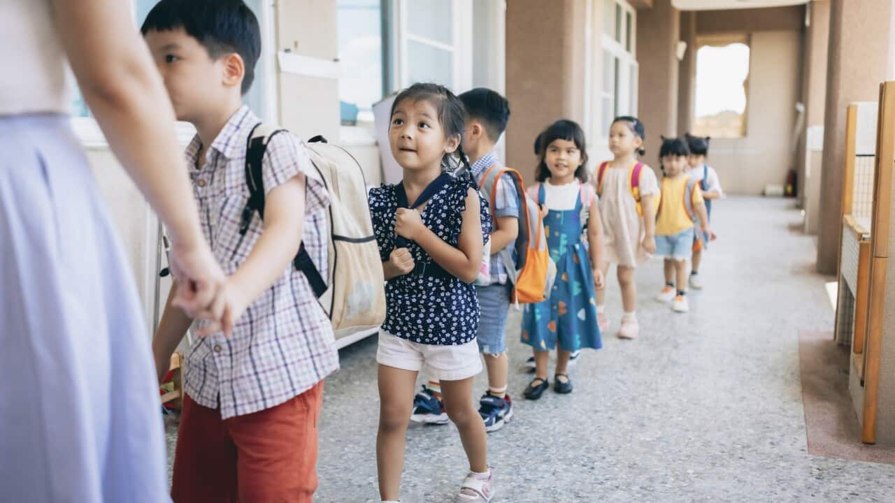 Preschool teacher guiding and arranging students waiting in line entering classroom