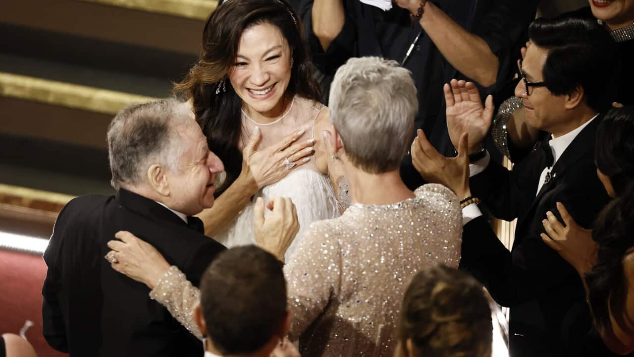 Michelle Yeoh smiles and hugs nearby actors after winning the Oscar for Best Actress.
