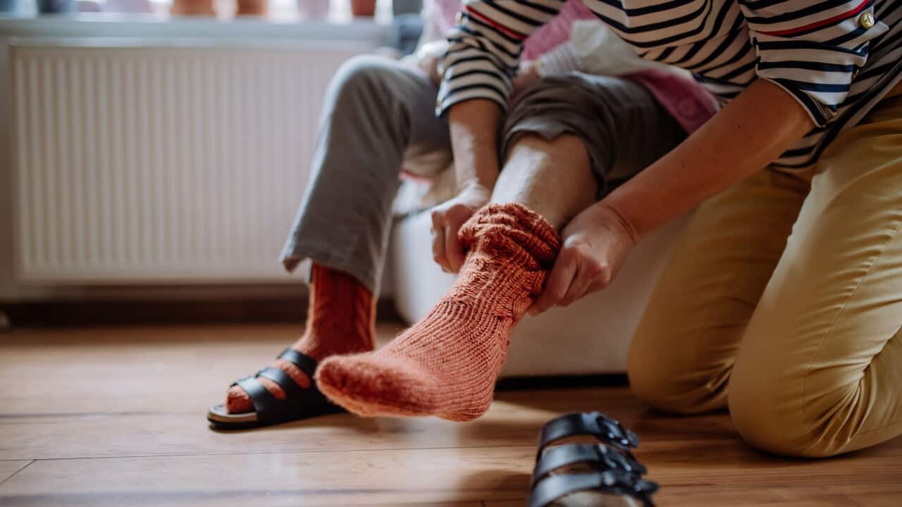 Close-up of healthcare worker putting on warm socks to senior woman.